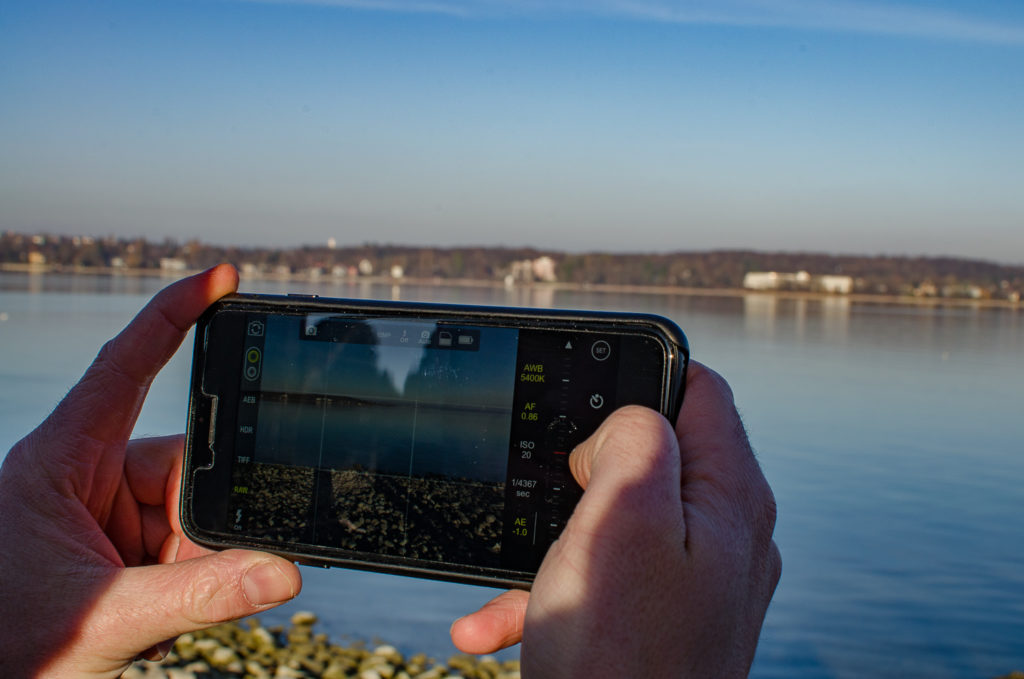 iPhone in den Händen mit Blick auf See & App auf Display
